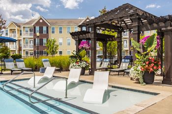 A pool with chairs and a pergola in front of a building